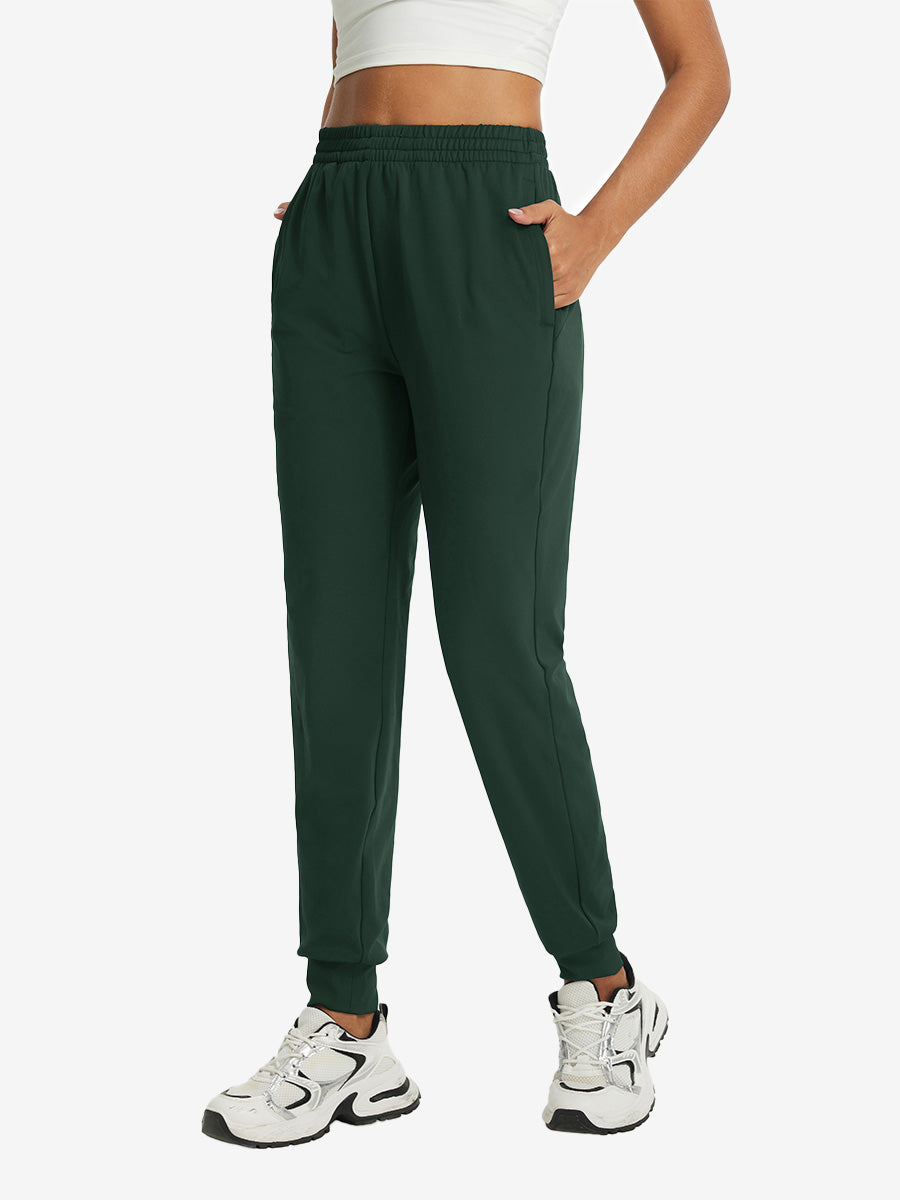 Model with hand in pocket wearing lightweight women's stretchy joggers sweatpants in forest green.