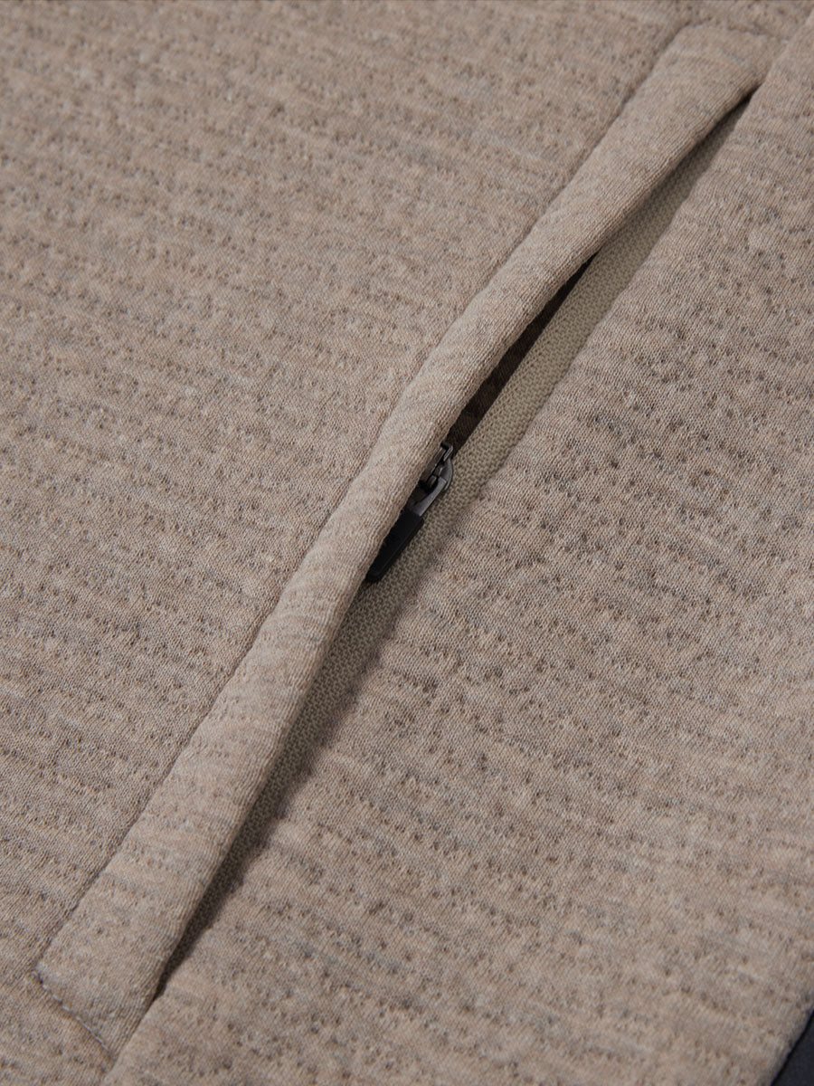 Close-up of jacket pocket showing fine stitching and insulation detail, textured insulated winter jacket, light brown heather.