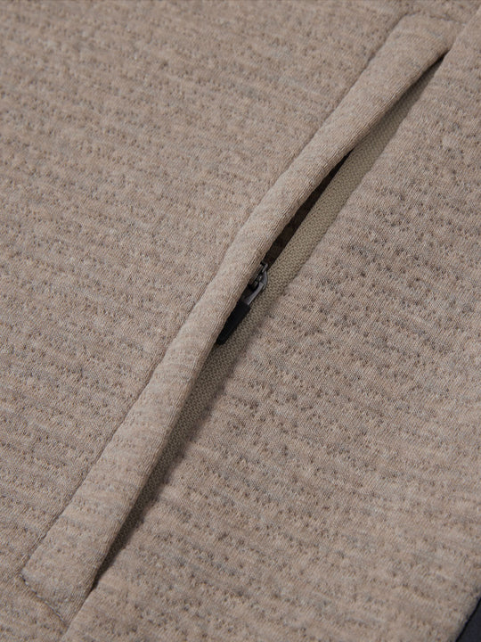 Close-up of jacket pocket showing fine stitching and insulation detail, textured insulated winter jacket, light brown heather.