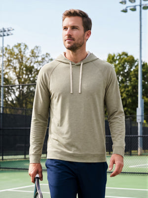 Front upper body angled shot of model wearing  taupe heather heather midlayer golf hoodie, holding a racket in one hand on the court